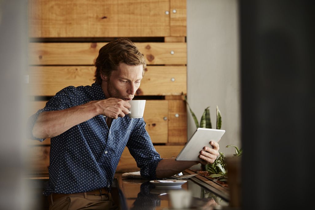 Mann trinkt perfekt zubereiteten Filterkaffee während er am Tablet liest