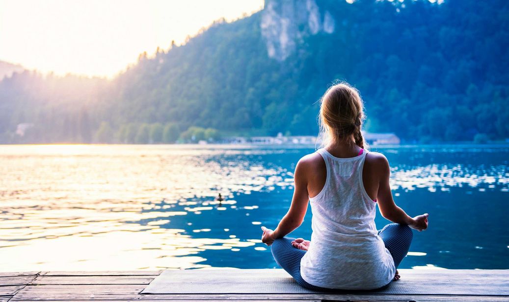 Eine Frau sitzt meditierend an einem See