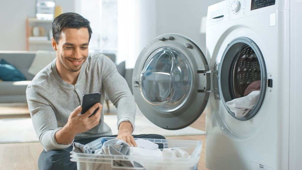 Mann mit Handy vor der Waschmaschine