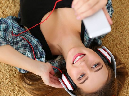 Eine Frau liegt auf dem Rücken am Boden und hört über ihr Smartphone Musik