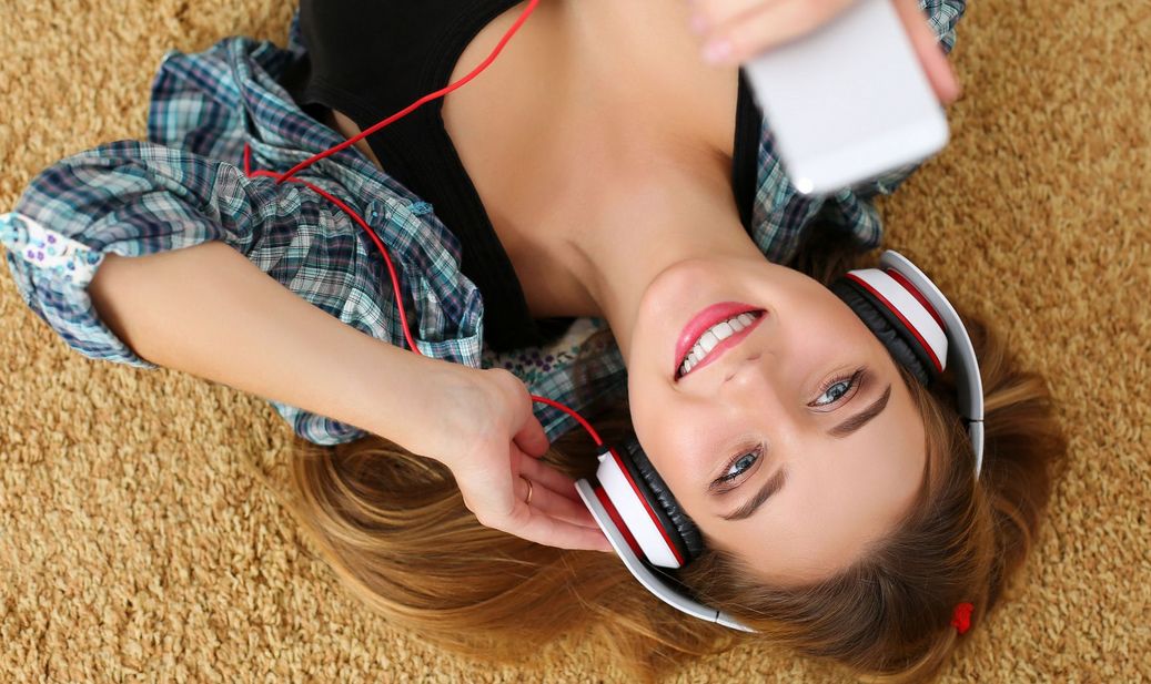 Eine Frau liegt auf dem Rücken am Boden und hört über ihr Smartphone Musik