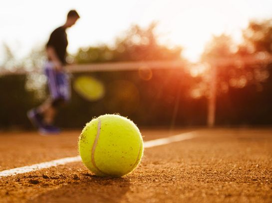 Ein Tennisball und -schläger liegen am Boden.